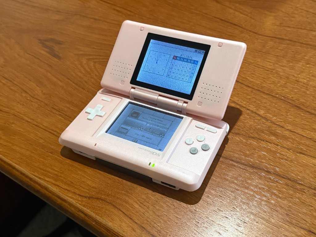 Original DS in a new pink shell, opened and powered on with both screens working.