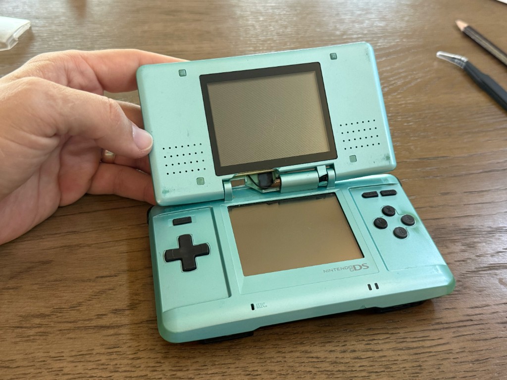 The same original DS opened, with the top half hanging from a broken hinge and a brittle shell.