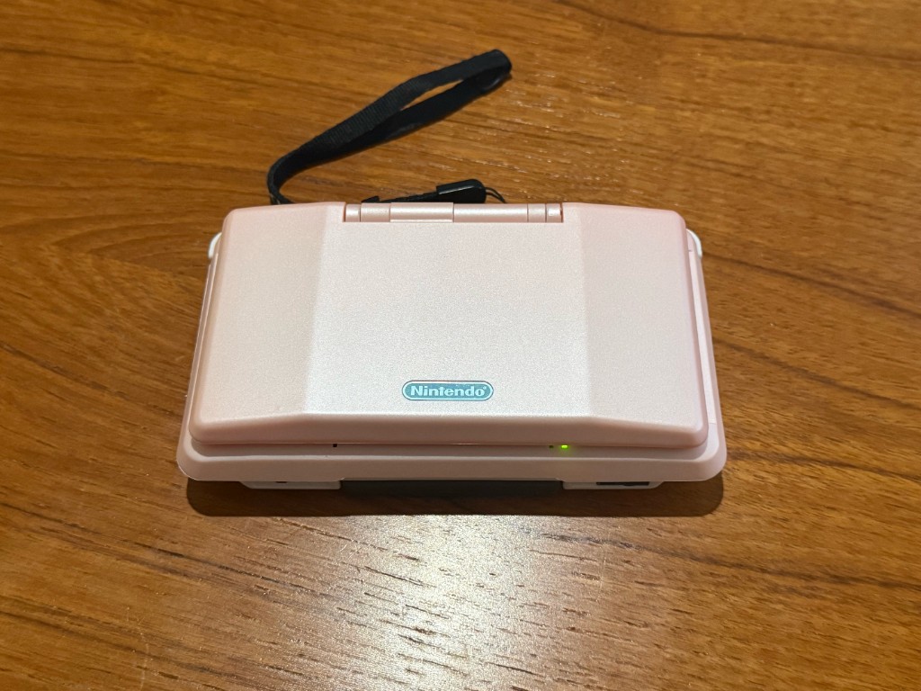 The same original DS closed in the new pink shell, with the power light on.