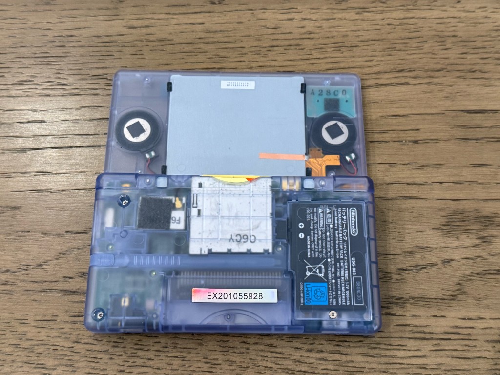 The back of a clear DS Lite, with the battery and board visible through the shell.