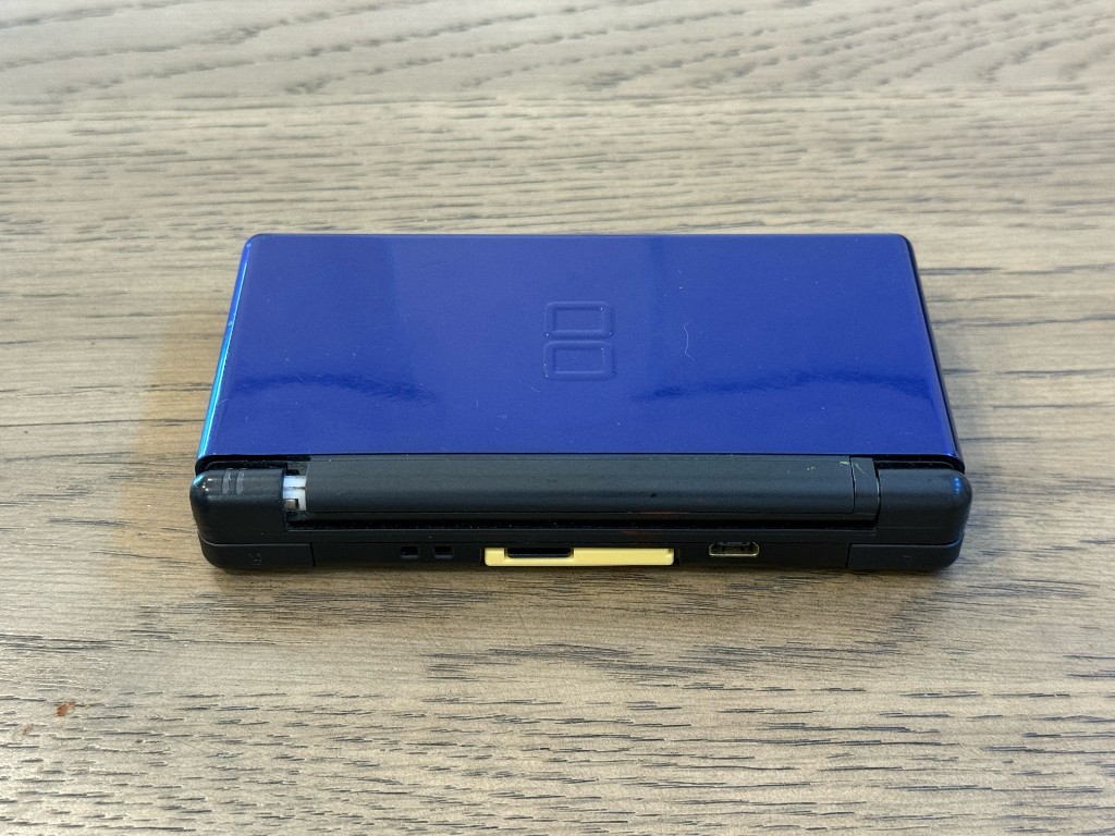 A closed blue and black DS Lite before a reshell, with a worn hinge.
