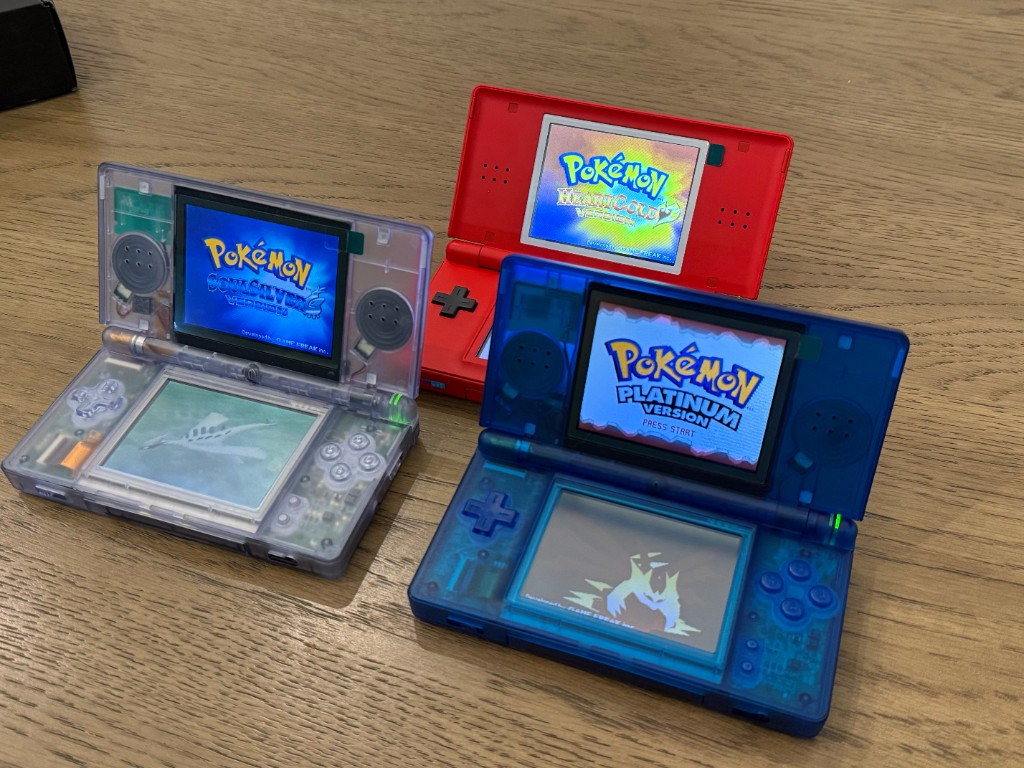 Three reshelled DS Lites powered on, showing Pokémon SoulSilver, HeartGold, and Platinum.