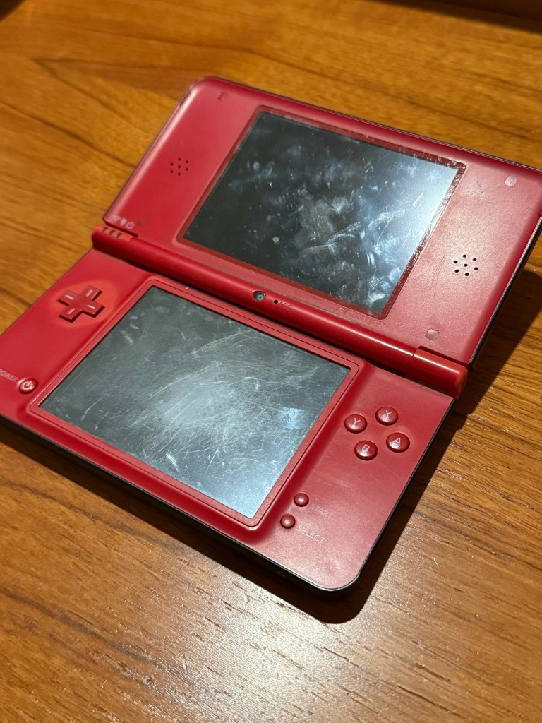 The same red DSi XL opened, with both screens heavily scratched.