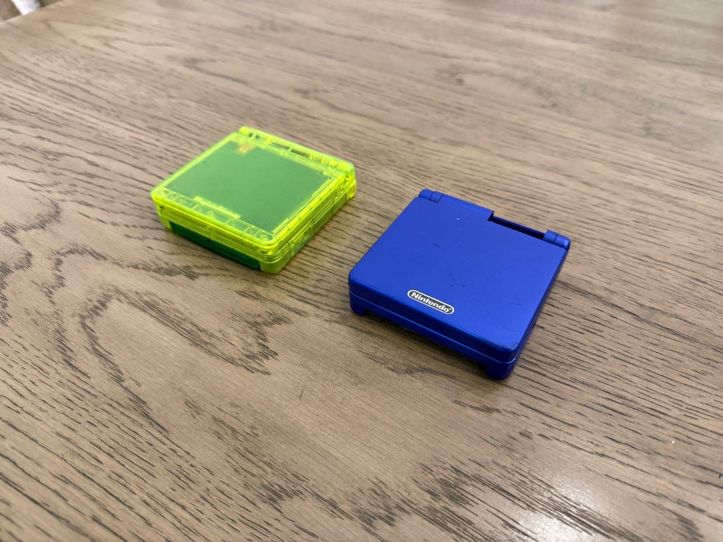 Two closed GBA SP shells: a clear lime-green shell and a solid blue shell.