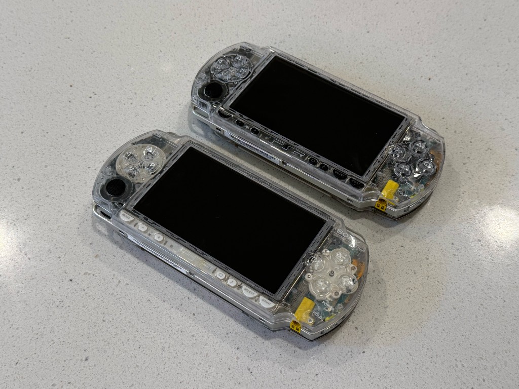 Two PSP 1000s rebuilt in clear shells, sitting side by side.