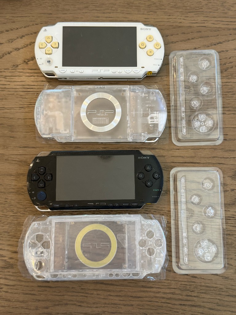 Two PSP 1000s, one white and one black, laid out with new clear shells and clear buttons.
